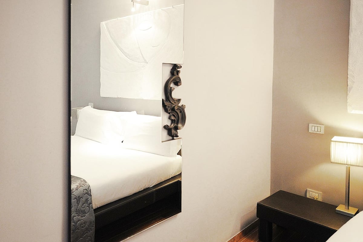 Een hotelkamer met een bed, nachtkastje, lamp en spiegel.