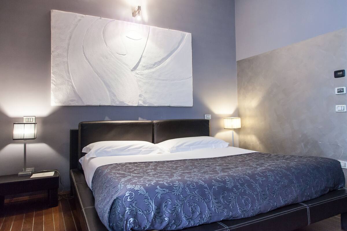 Een hotelkamer met een bed, twee bedlampen, een kunstwerk aan de muur en een gestructureerde wand.