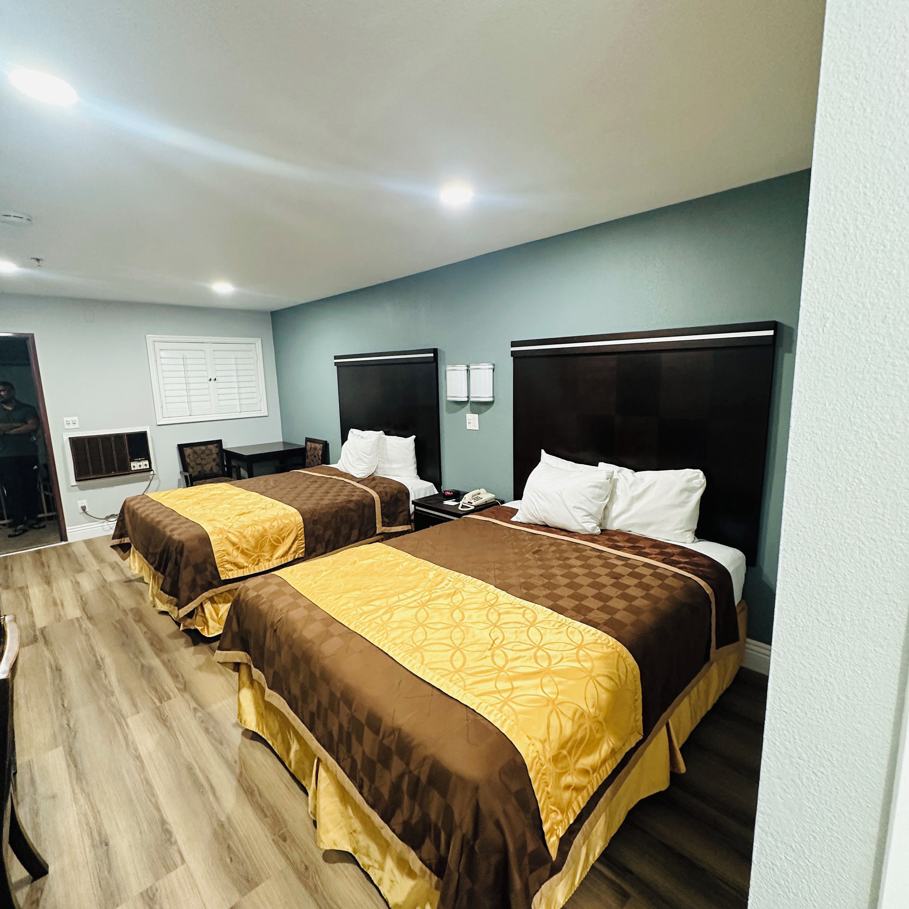 A hotel room with two beds, a desk, a chair, and a window with blinds.