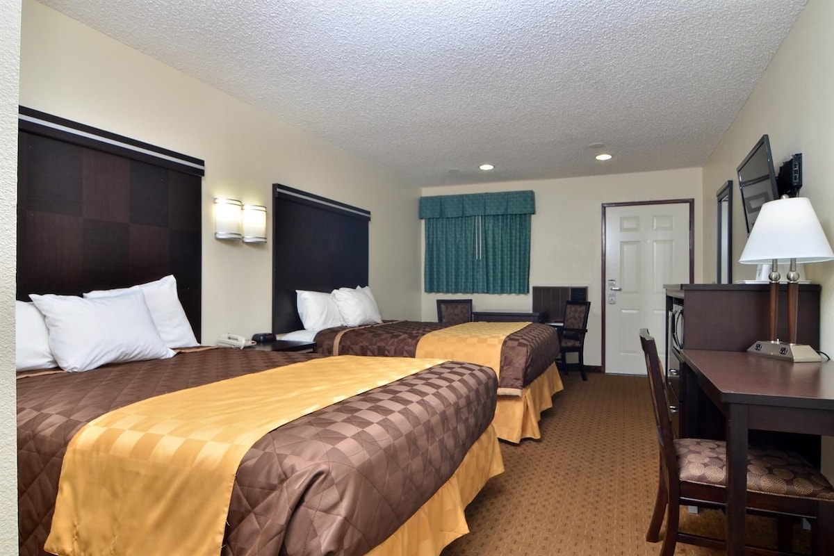 A hotel room with two beds, a desk, a chair, a TV, and a door.