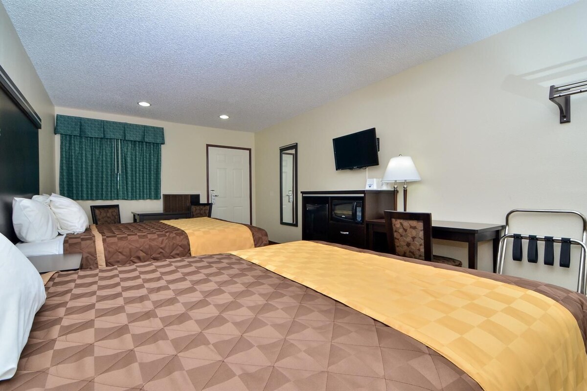 A hotel room with two beds, a desk, a chair, a TV, and a lamp.