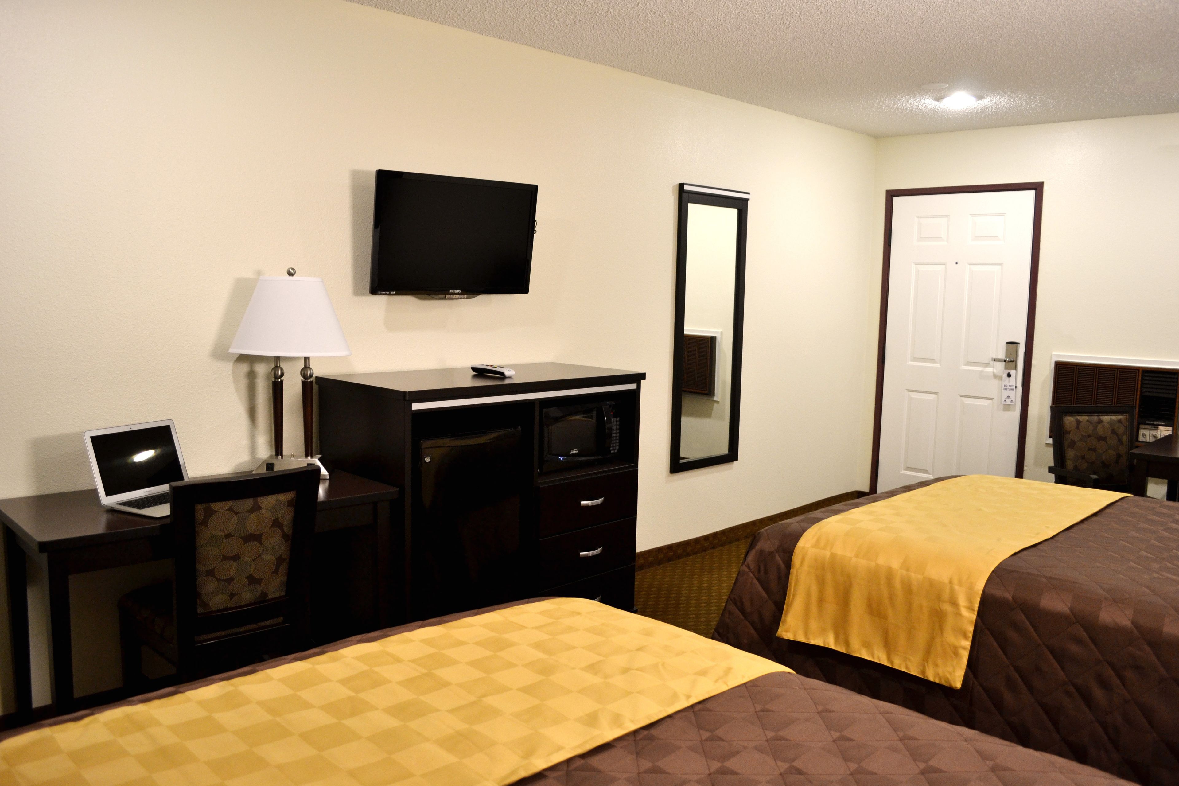 A hotel room with two beds, a desk with a computer, a TV, a mirror, and a door.