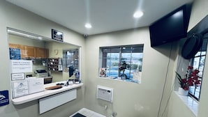 A reception area with a counter, a large mirror, a window with a view of the outside, and a mounted television.