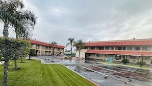 A hotel with a red roof, a parking lot, and a grassy area with trees.