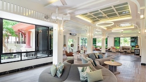 Un vestíbulo amplio con diseño moderno, que cuenta con un gran espacio de estar con sofás y sillones, un mostrador de recepción y ventanas grandes con vistas al exterior.