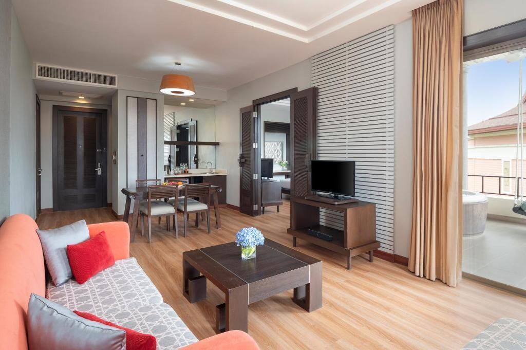 Ein modernes Hotelzimmer mit einer Couch, einem Esstisch, einem Fernseher und einem Balkon mit Blick.