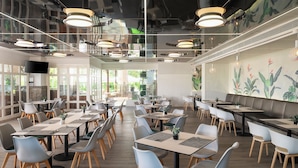 Un restaurante amplio con varias mesas y sillas, ventanas grandes y un diseño de techo moderno.