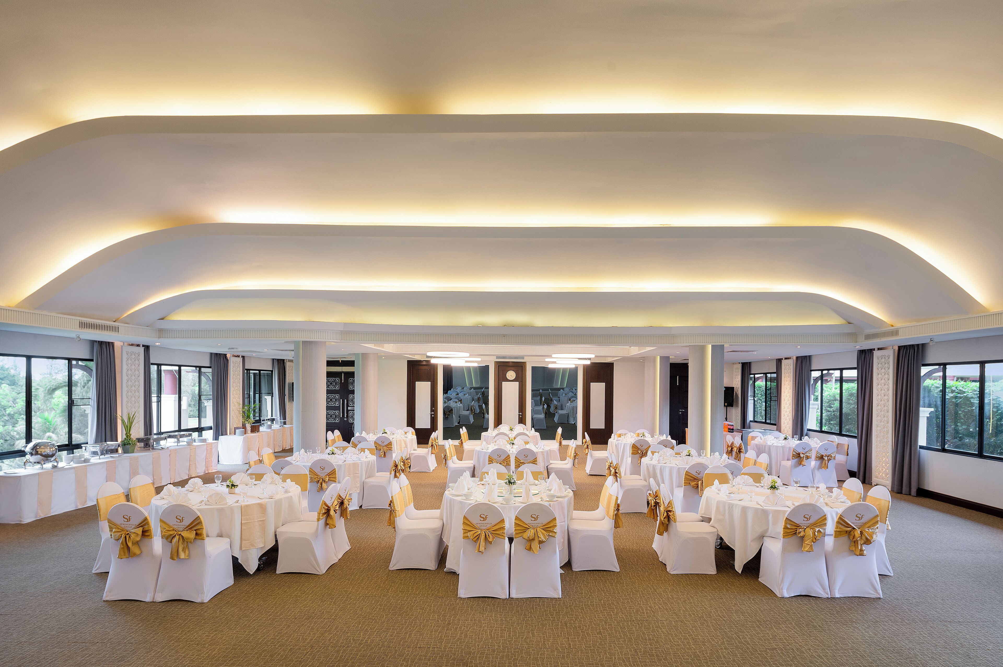 Un salón de banquetes con mesas redondas, manteles blancos y fajas doradas.