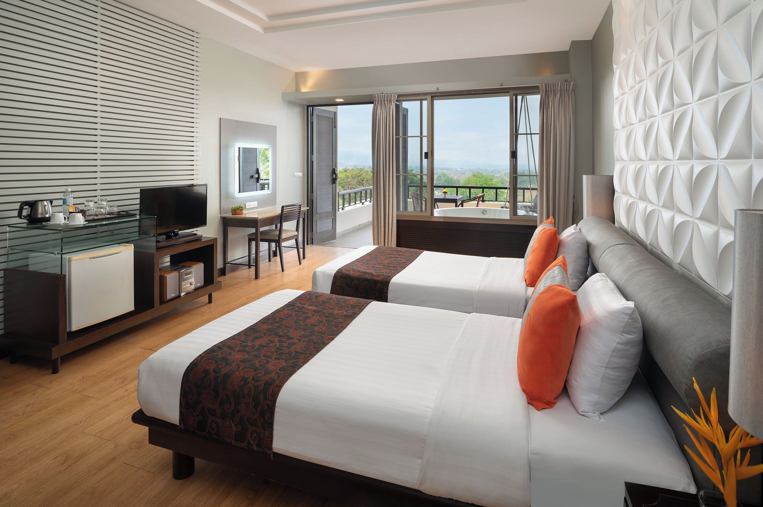 A hotel room with two beds, a desk, a TV, and a balcony with a view.