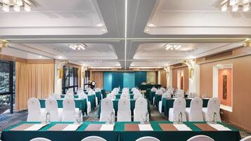 A conference room with rows of tables and chairs, a stage, and a large window.