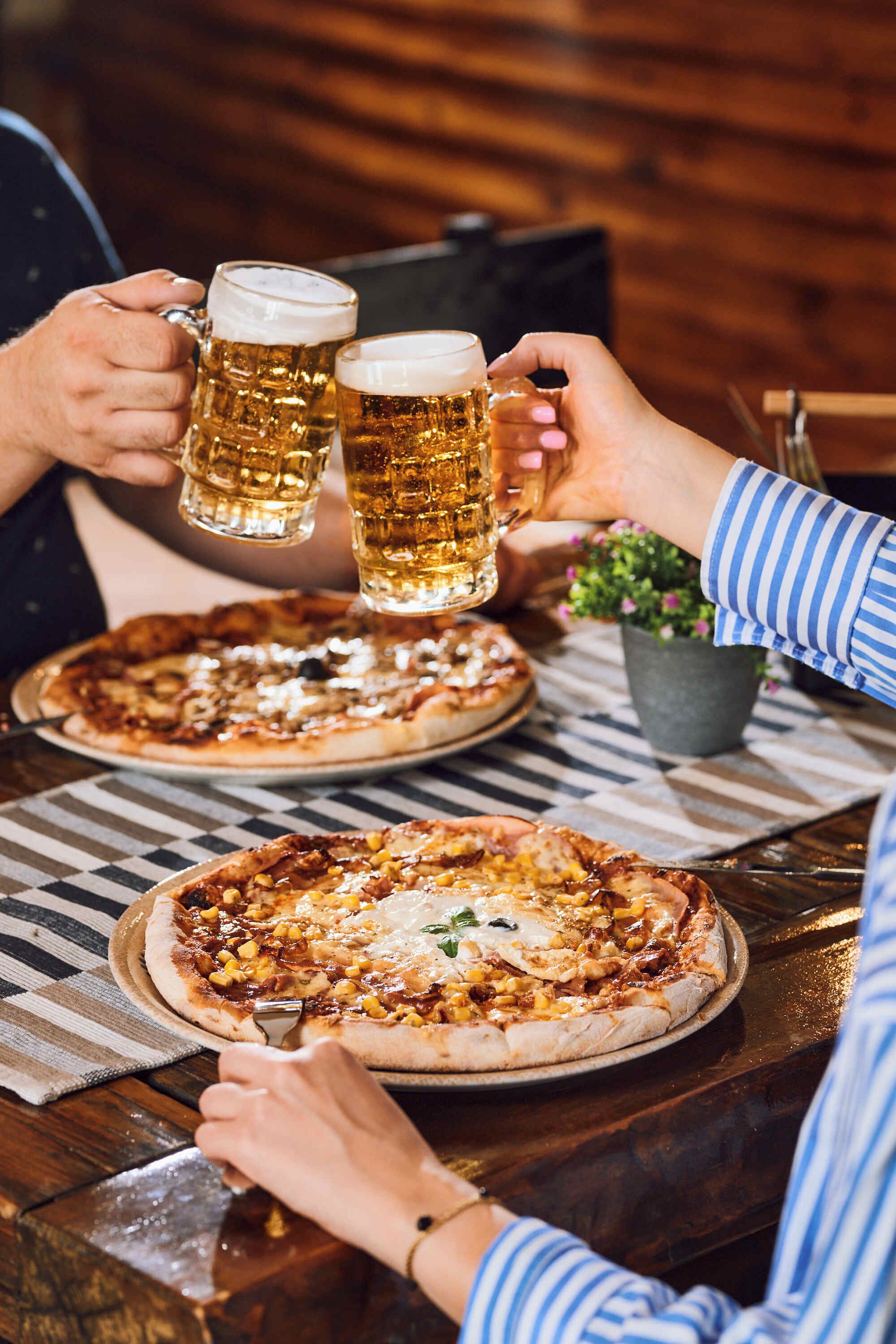 A dining table with two pizzas and two beer mugs.