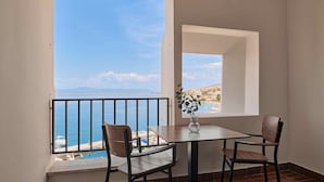 A balcony with a table and chairs, a vase with a plant, and a view of the sea and distant buildings. - Hotel Selce  (Crikvenica)