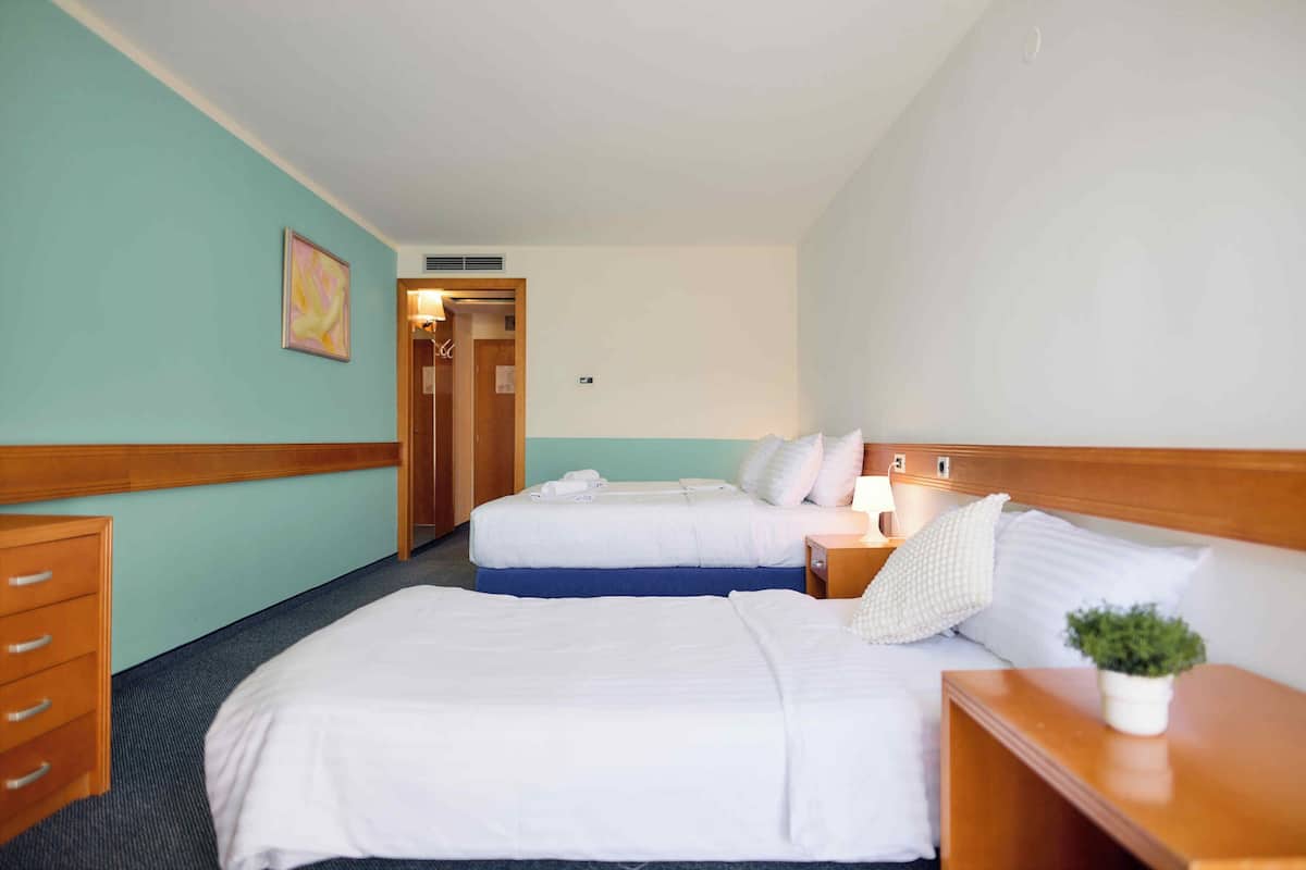 A hotel room with two beds, a wooden dresser, a small plant, and a painting on the wall.