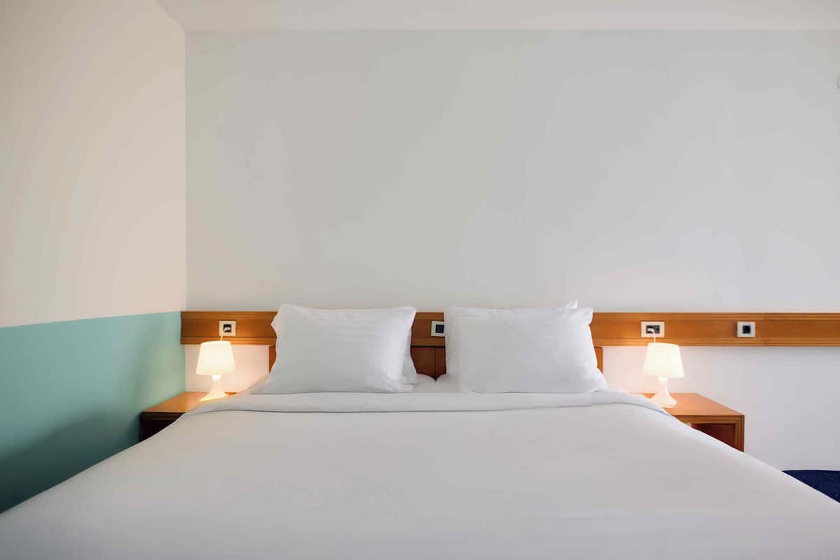 A hotel room with a large bed, two bedside tables with lamps, and a wooden headboard.