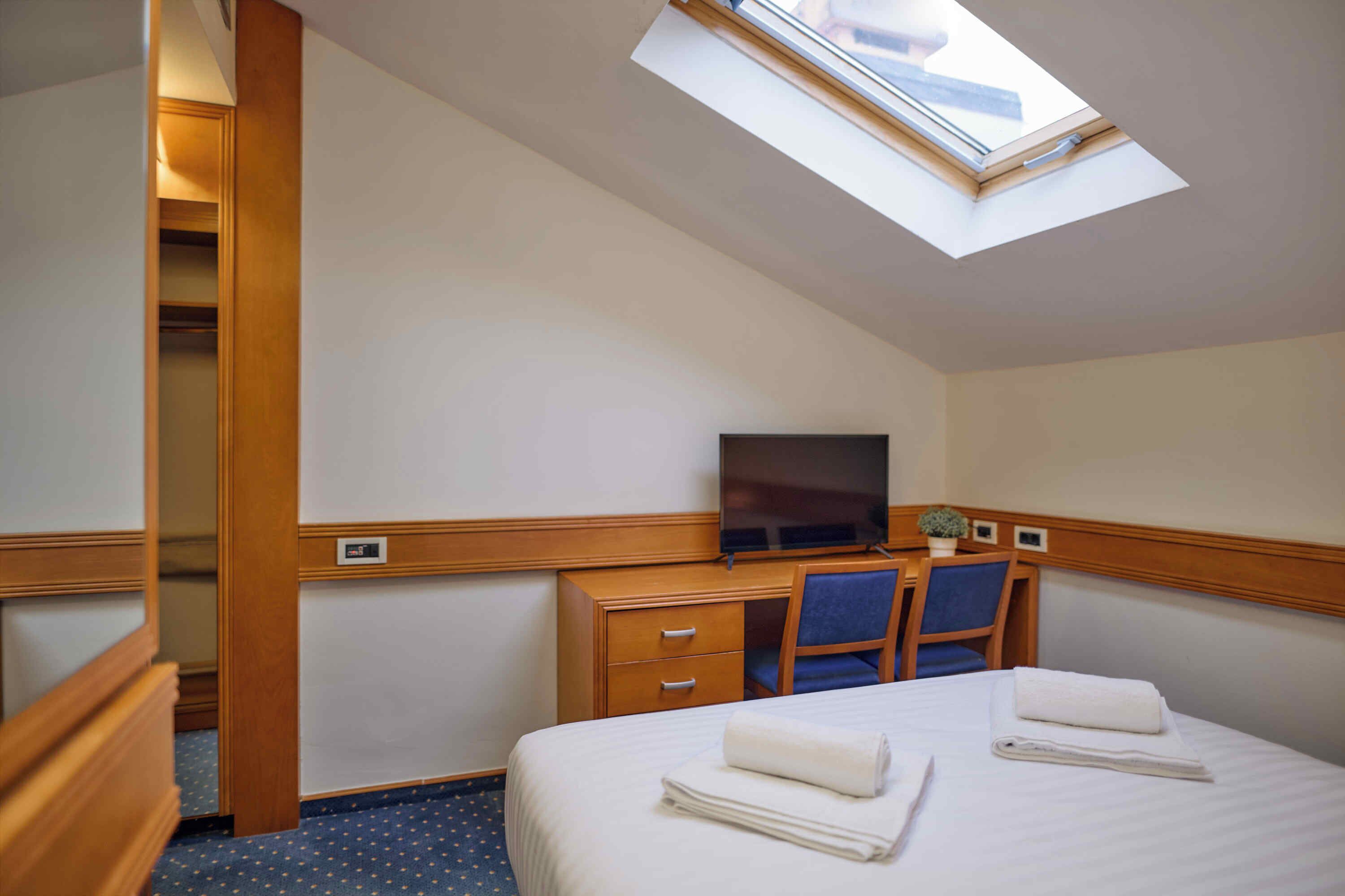 Une chambre d’hôtel comprenant un lit, un bureau avec une chaise, une télévision et une lucarne.