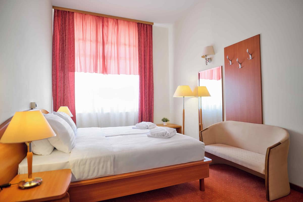 A hotel room with a bed, a chair, a nightstand, and a lamp.
