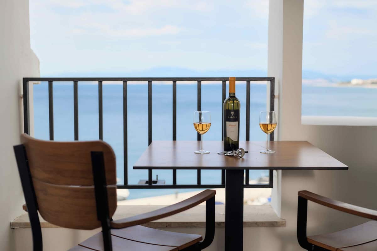 A balcony with a table, two chairs, a bottle of wine, and two glasses.