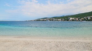 A beach with clear turquoise water, a sandy shore, and a town in the background. - Hotel Selce  (Crikvenica)