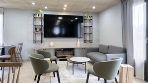 A modern living room with a flat-screen TV, grey sofa, green chairs, and a fireplace. - Campanile NATURE - Mont de Marsan (Mont-de-Marsan)