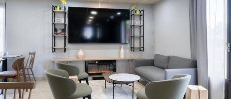 A modern living room with a flat-screen TV, grey sofa, green chairs, and a fireplace.