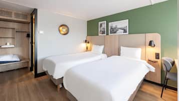 Habitación de hotel con dos camas, un armario de madera, una silla y una pared verde con dos cuadros enmarcados.