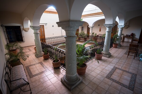 An indoor courtyard with tiled flooring, stone columns, potted plants, and a metal railing. - Hotel Parador San Agustin (Oaxaca)