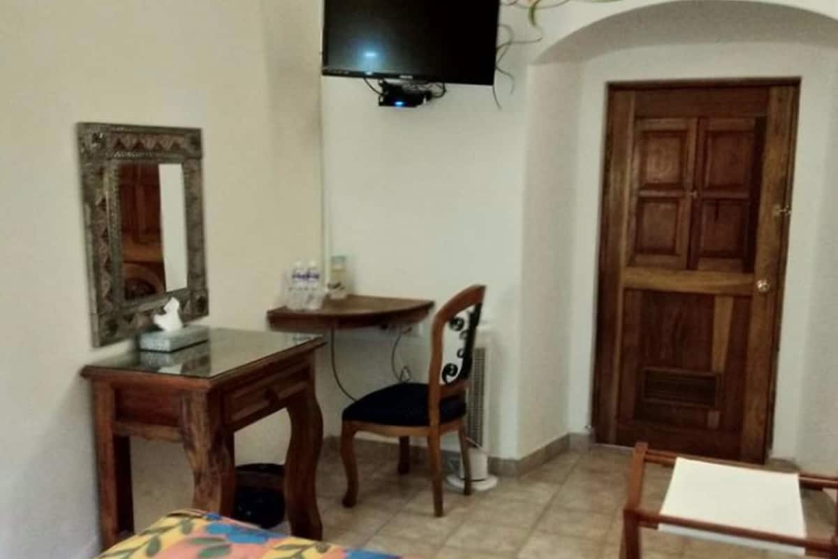 A room with a bed, a desk, a chair, a television mounted on the wall, and a wooden door.