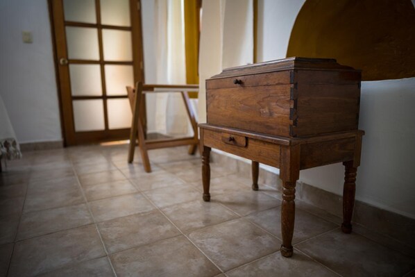 A wooden chest of drawers in a room with tiled flooring and a wooden door with glass panels. - Hotel Parador San Agustin (Oaxaca)