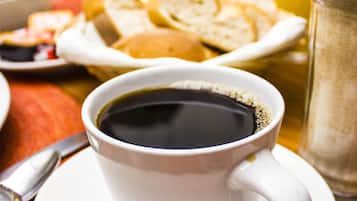 A cup of black coffee on a white saucer with a spoon beside it, a salt shaker, and a glass of orange juice on a table.