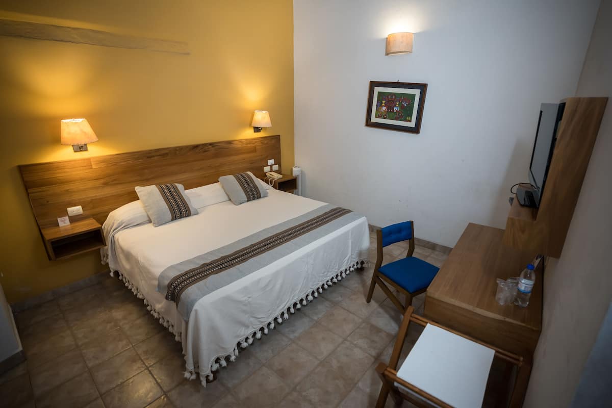 A hotel room with a bed, bedside lamps, a desk with a chair, and a framed picture on the wall.
