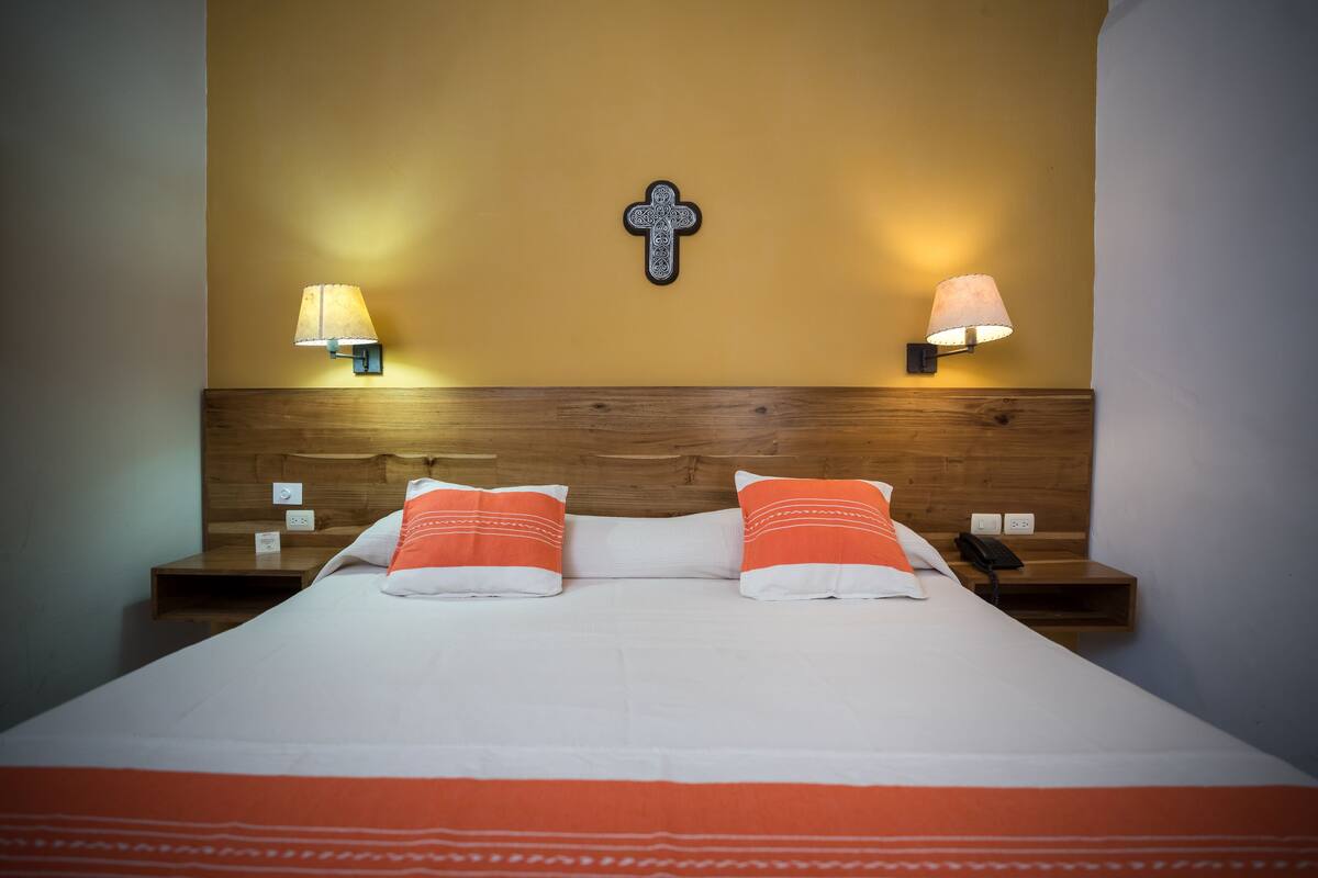 A neatly made bed with white and orange bedding, two bedside lamps, and a wooden headboard.