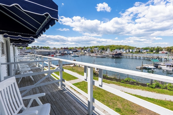 A wooden deck with white railings overlooking a marina with boats and a pier.