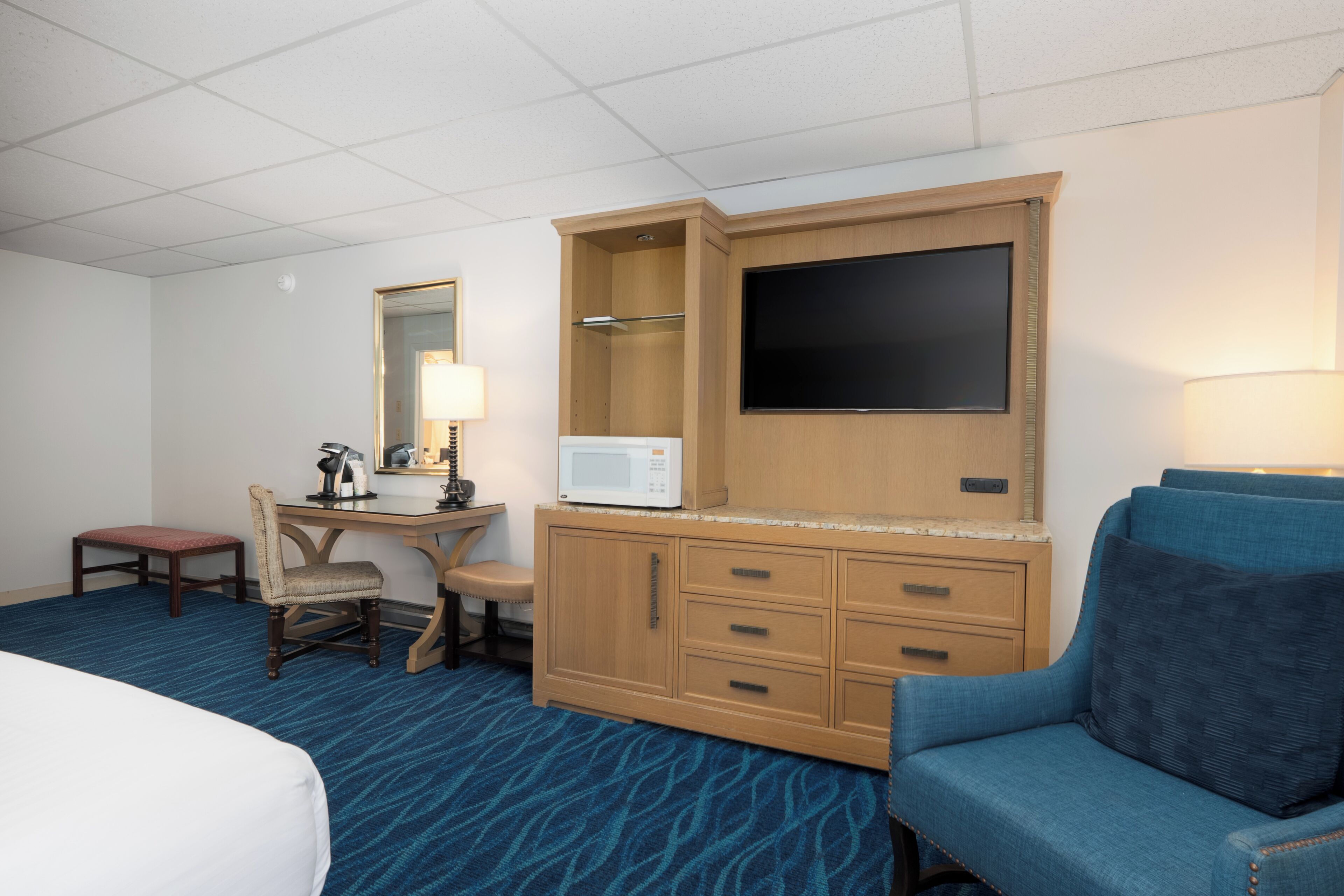 Quarto de hotel com cama, escrivaninha com computador, micro-ondas, televisão, cadeira e sofá.