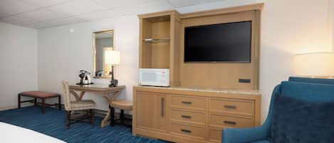 Quarto de hotel com cama, escrivaninha com computador, micro-ondas, televisão, cadeira e sofá.