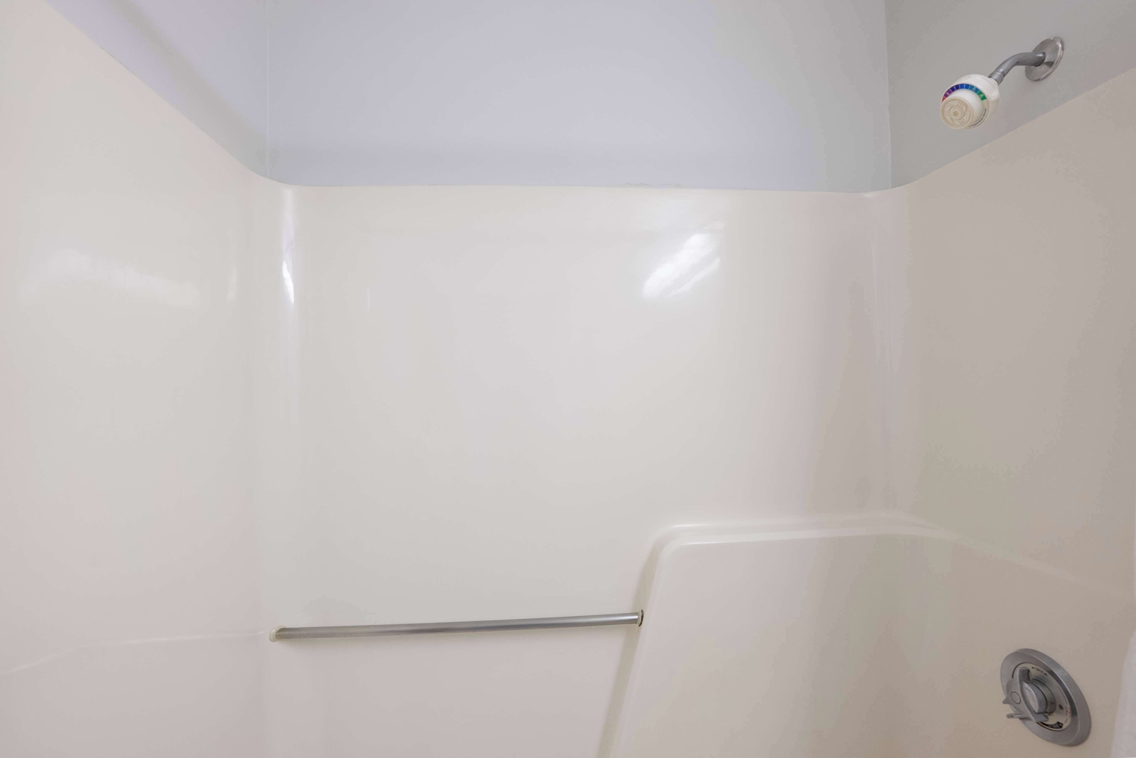 A bathroom with white walls, a shower with a chrome faucet, and a metal grab bar.