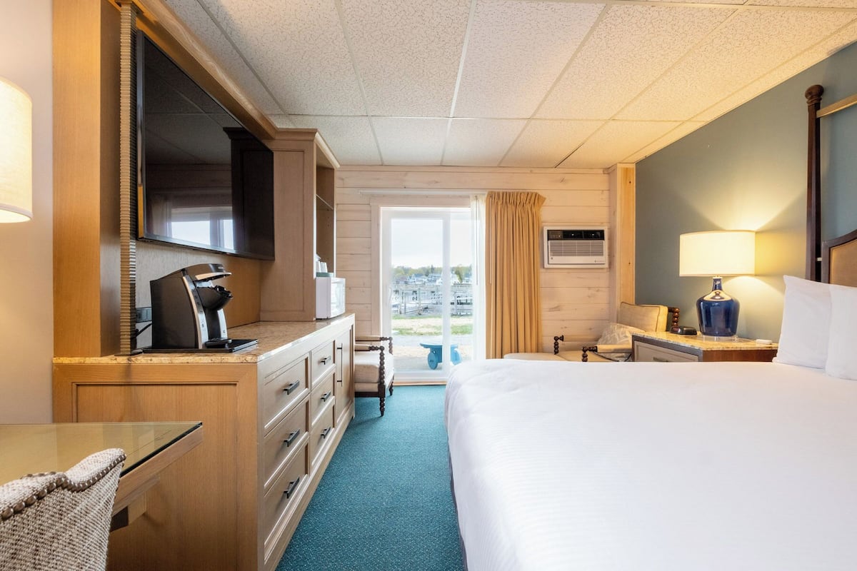 A hotel room with a bed, a desk, a dresser, a television, a coffee maker, and a window with curtains.