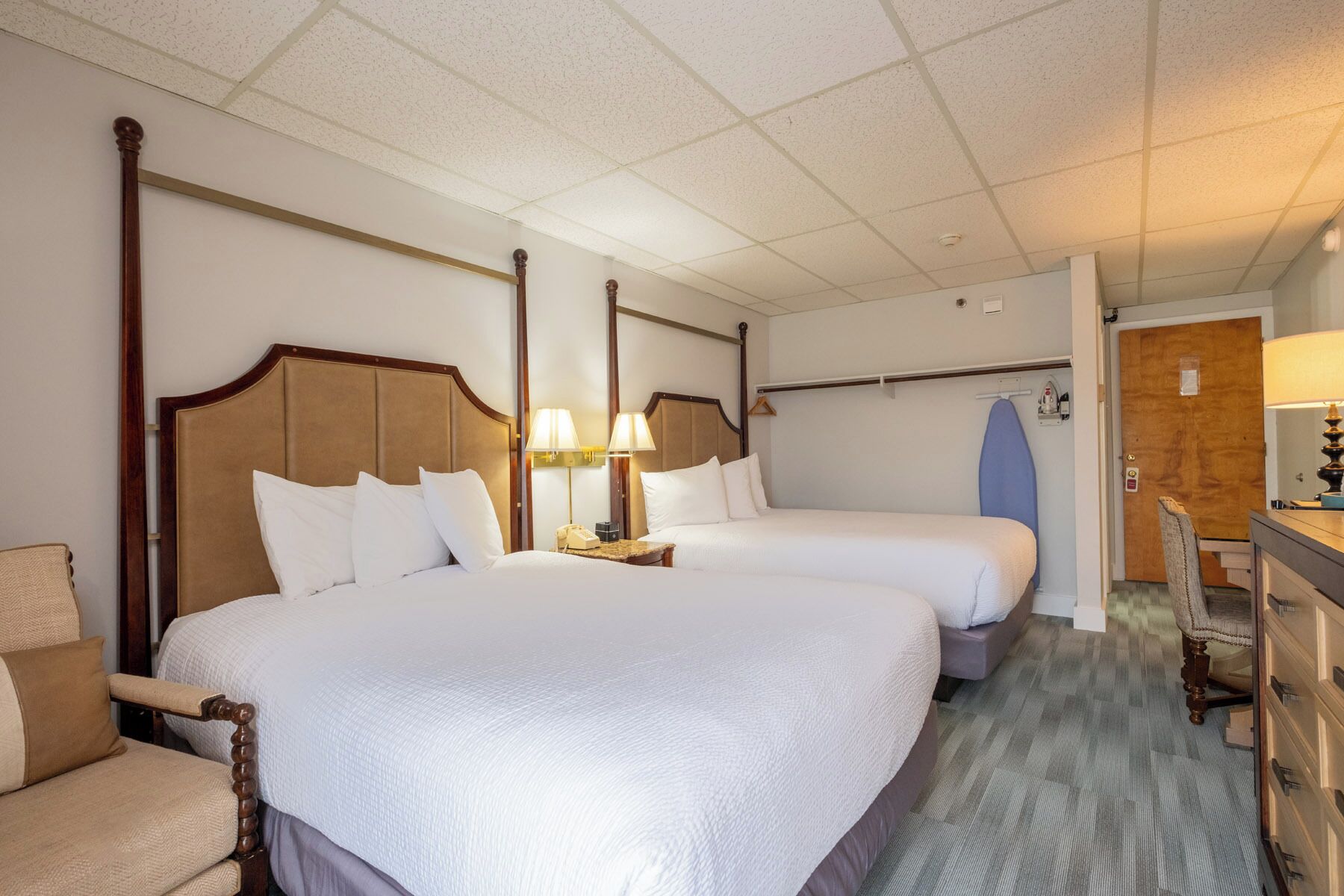 A hotel room with two beds, a desk, a chair, a wardrobe, and a door.