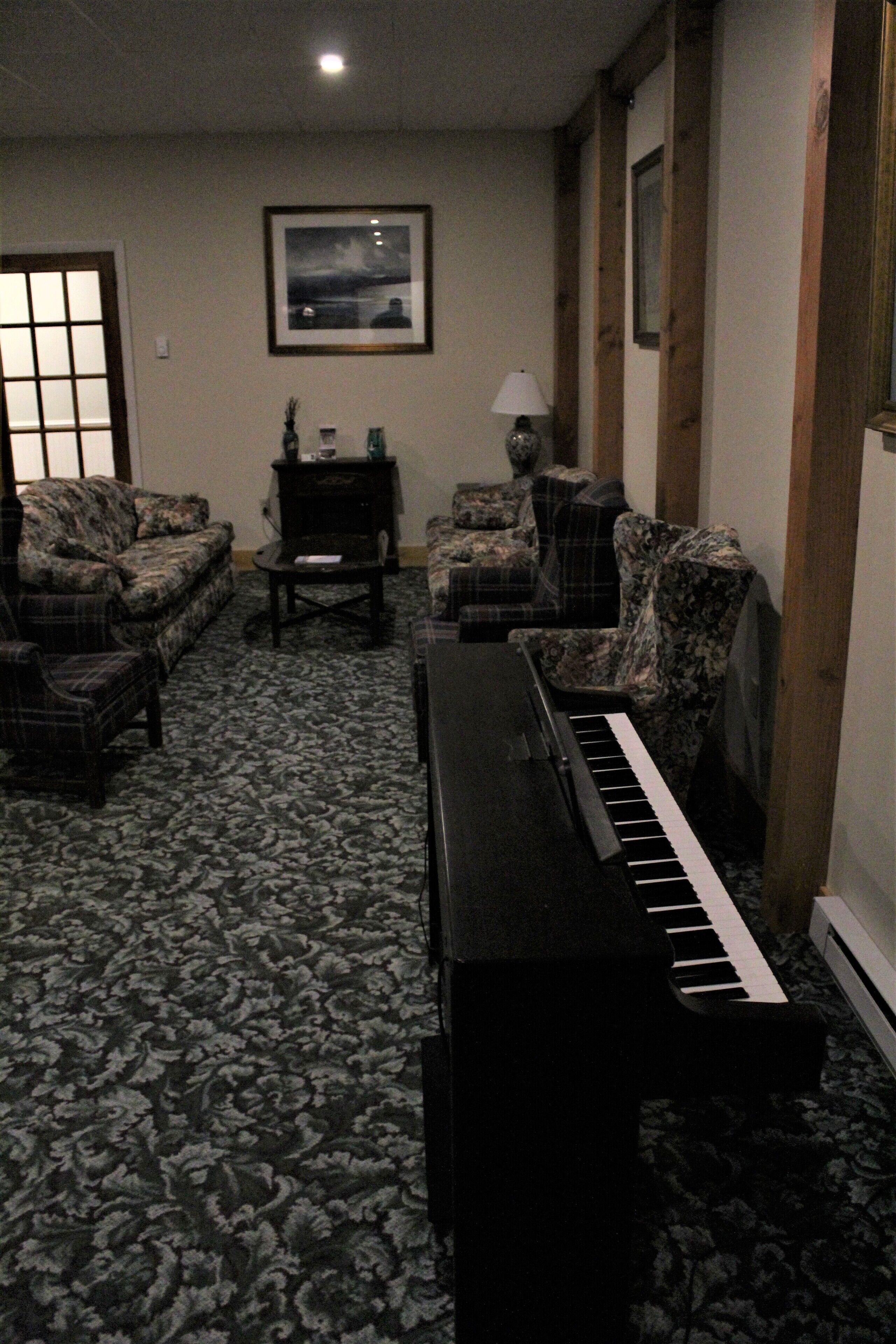 A living room with a piano, two sofas, a coffee table, and a lamp.