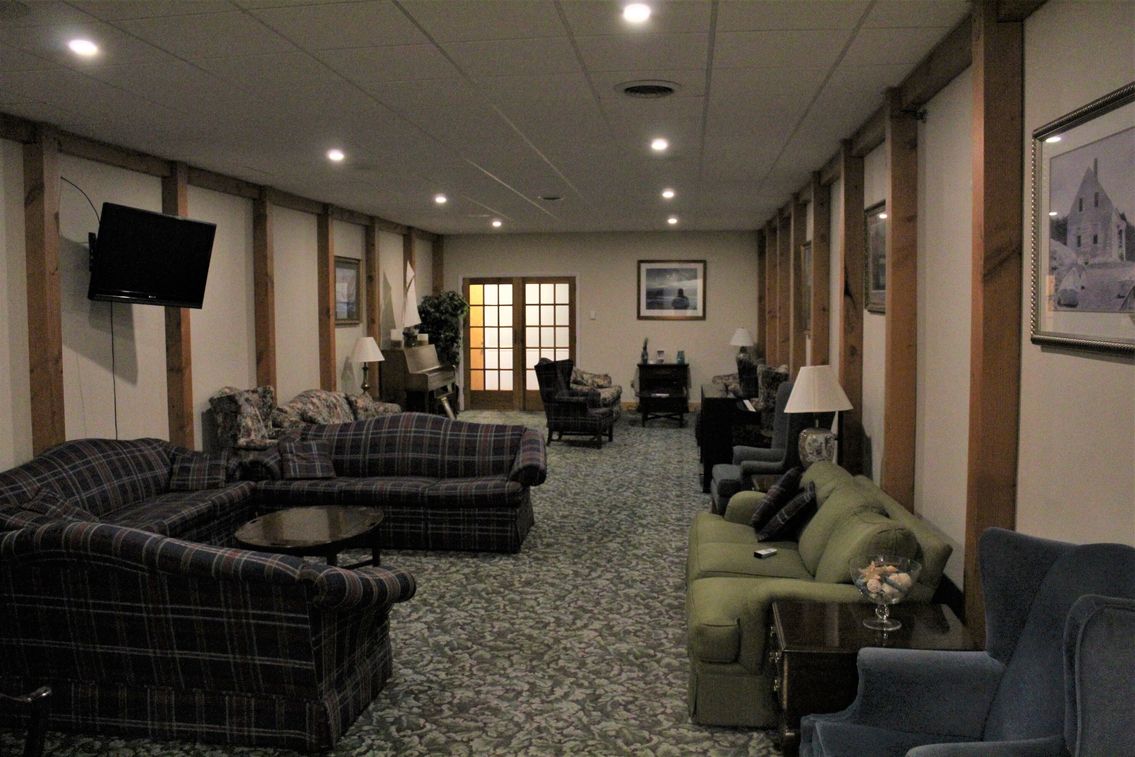 A spacious living room with a large sectional sofa, a smaller sofa, and a green armchair. There is a flat-screen TV mounted on the wall, a fireplace, and several framed pictures on the walls.