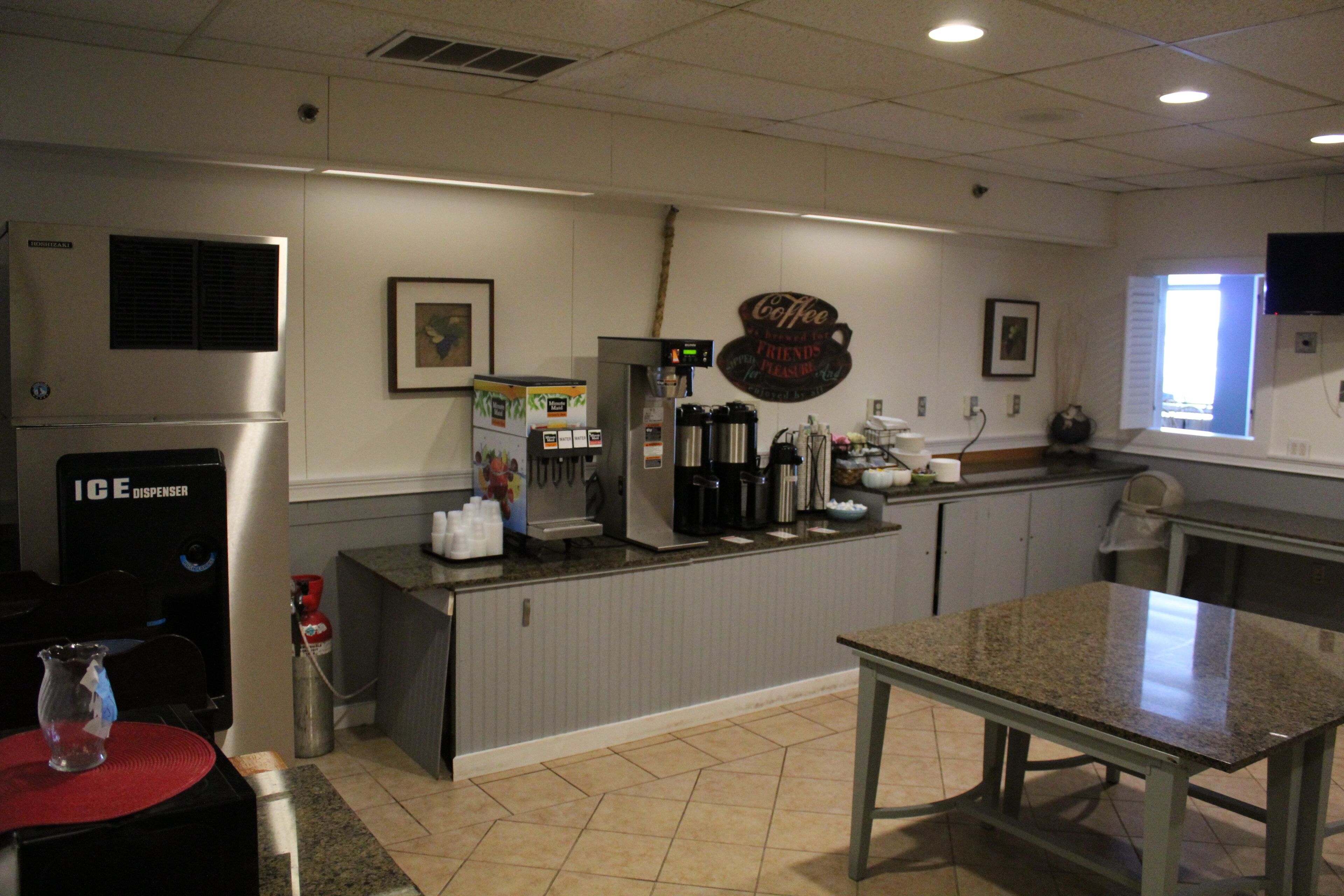 Uma área de cozinha com dispensador de gelo, cafeteira e uma placa que diz 'Coffee Friends'.