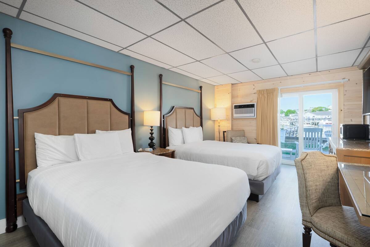 A hotel room with two beds, a desk, a chair, a TV, and a balcony with a view.