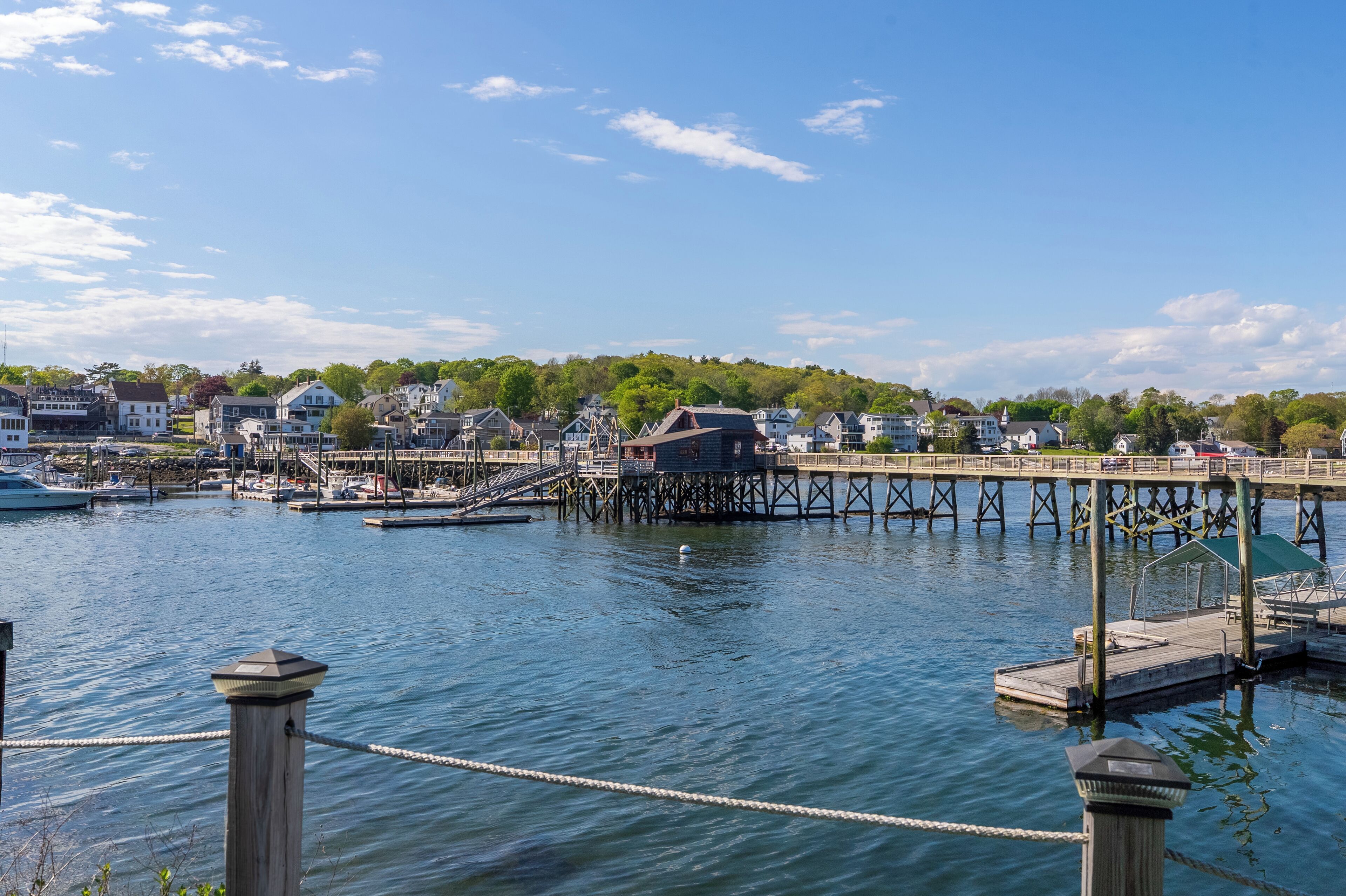 A waterfront marina with docked boats, a wooden pier, and residential buildings in the background.