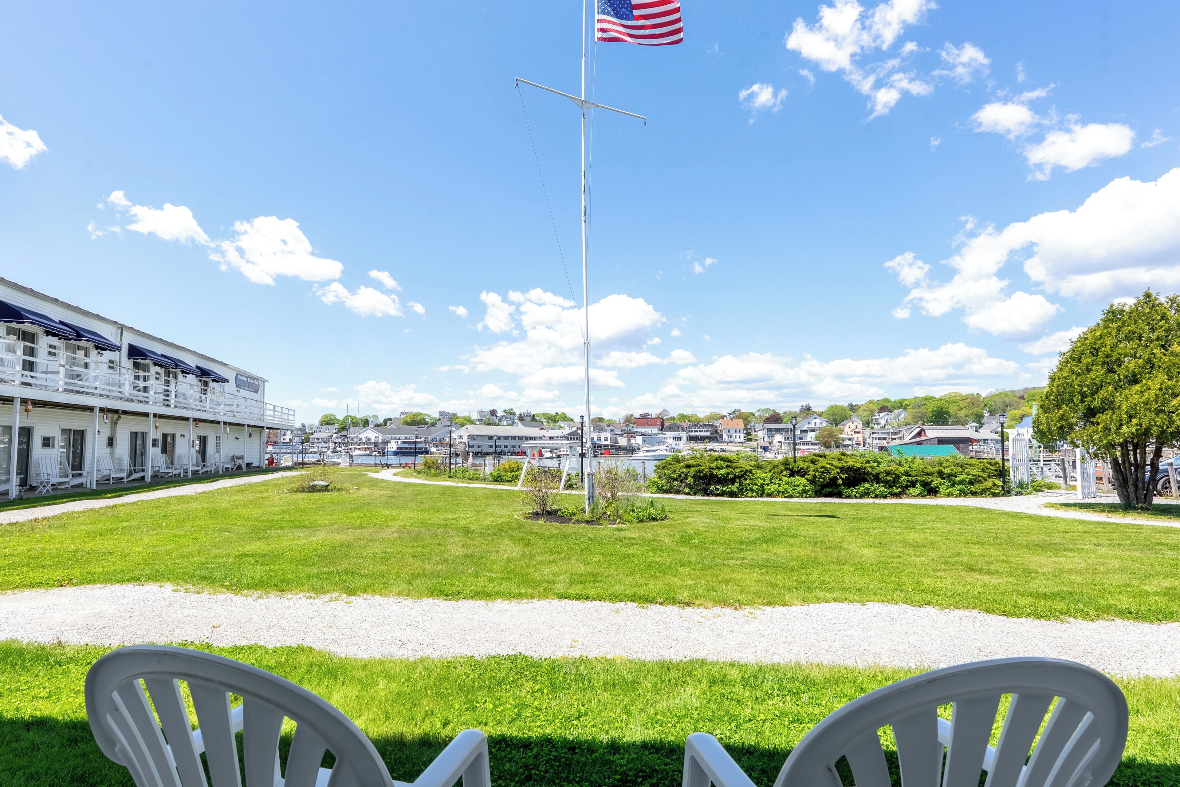 En græsplæne med flagstang og amerikansk flag, en bygning med hvid facade, og en klar himmel.