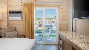 A room with a bed, a chair, a TV, an air conditioning unit, and a sliding glass door leading to an outdoor area with chairs and tables. - Boothbay Harbor Inn (Boothbay Harbor)