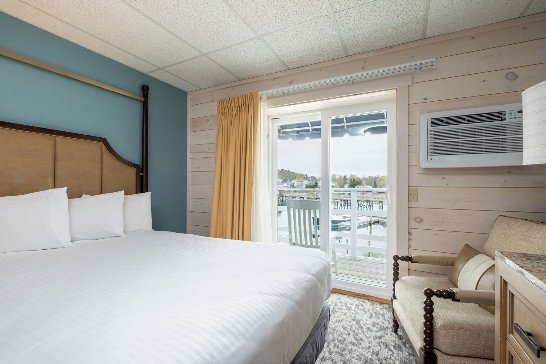 A hotel room with a bed, a chair, a window with a view, and an air conditioning unit.