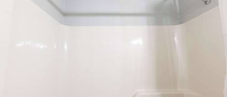 Ein Eckbereich eines Badezimmers mit weißen Wänden, einer Dusche und einem Handtuchhalter.