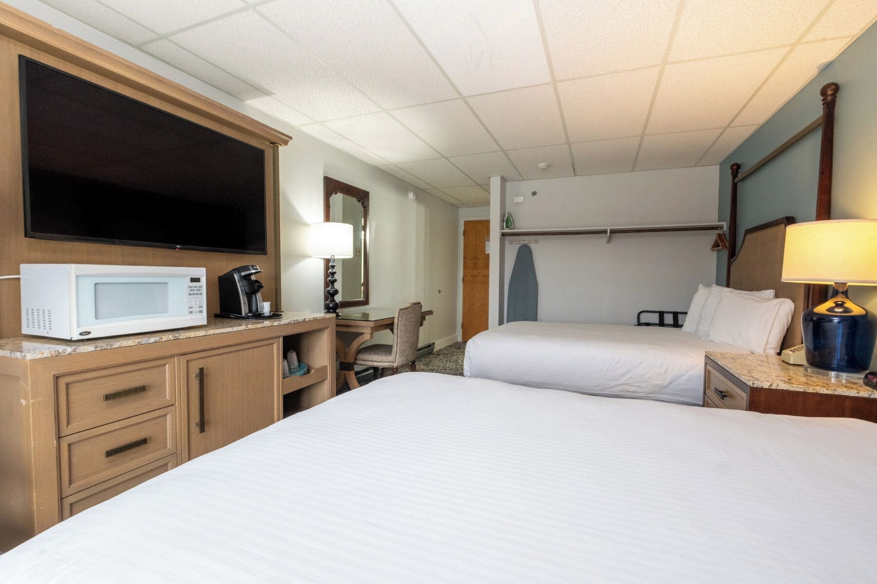 A hotel room with a bed, a desk with a microwave, a TV, and a lamp.