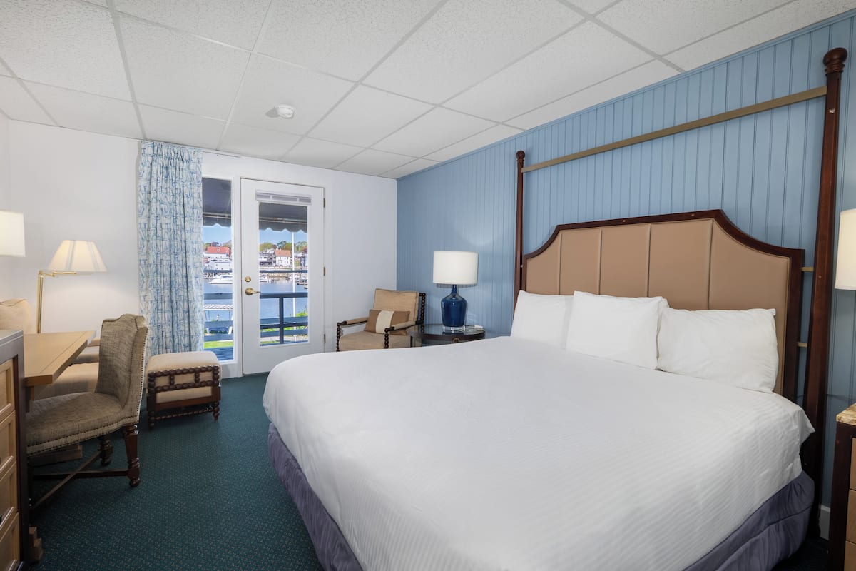 A hotel room with a large bed, two chairs, a desk, and a window with a view of the outside.