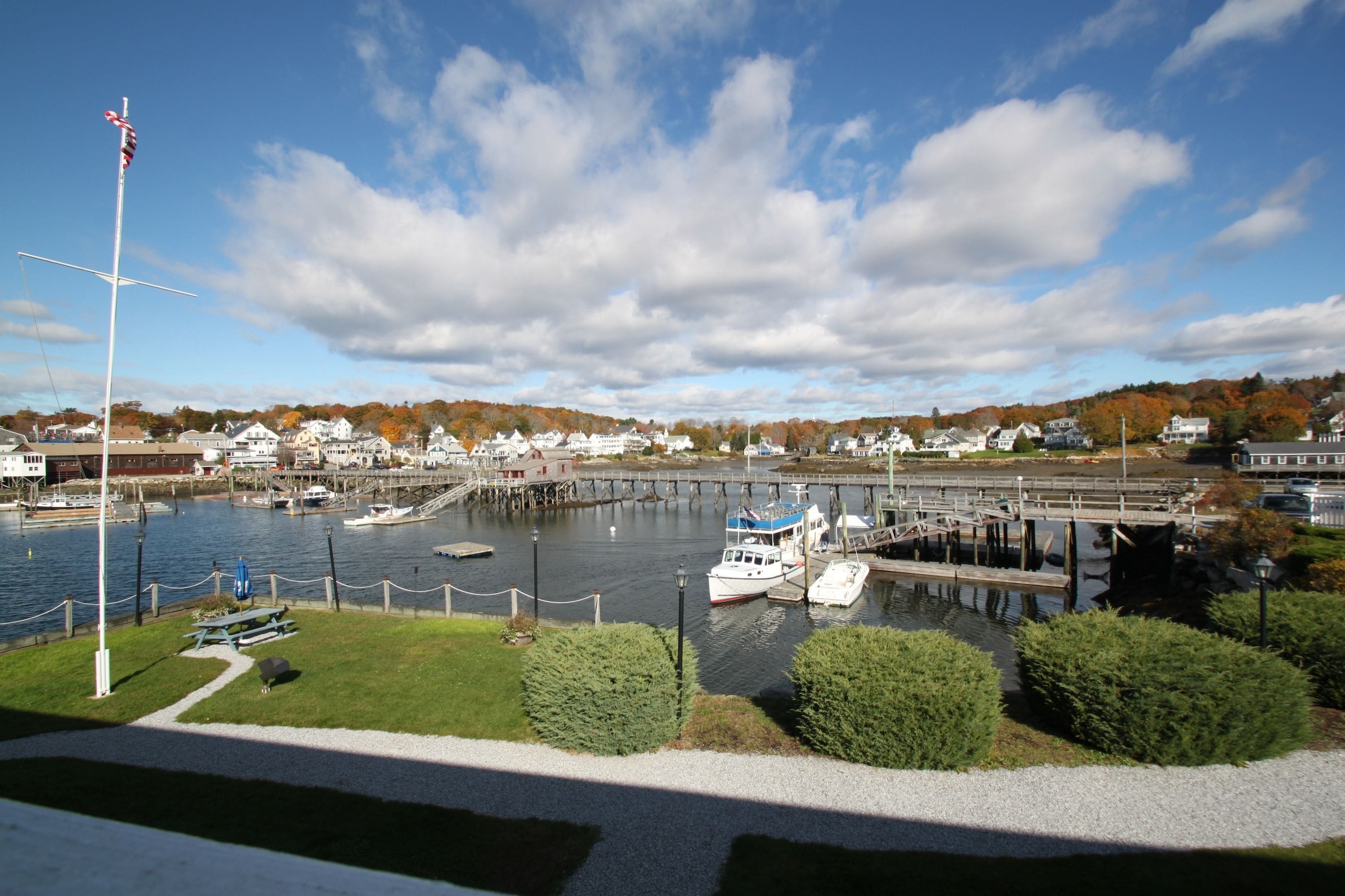 A harbor with boats docked, a flagpole, and houses in the background.