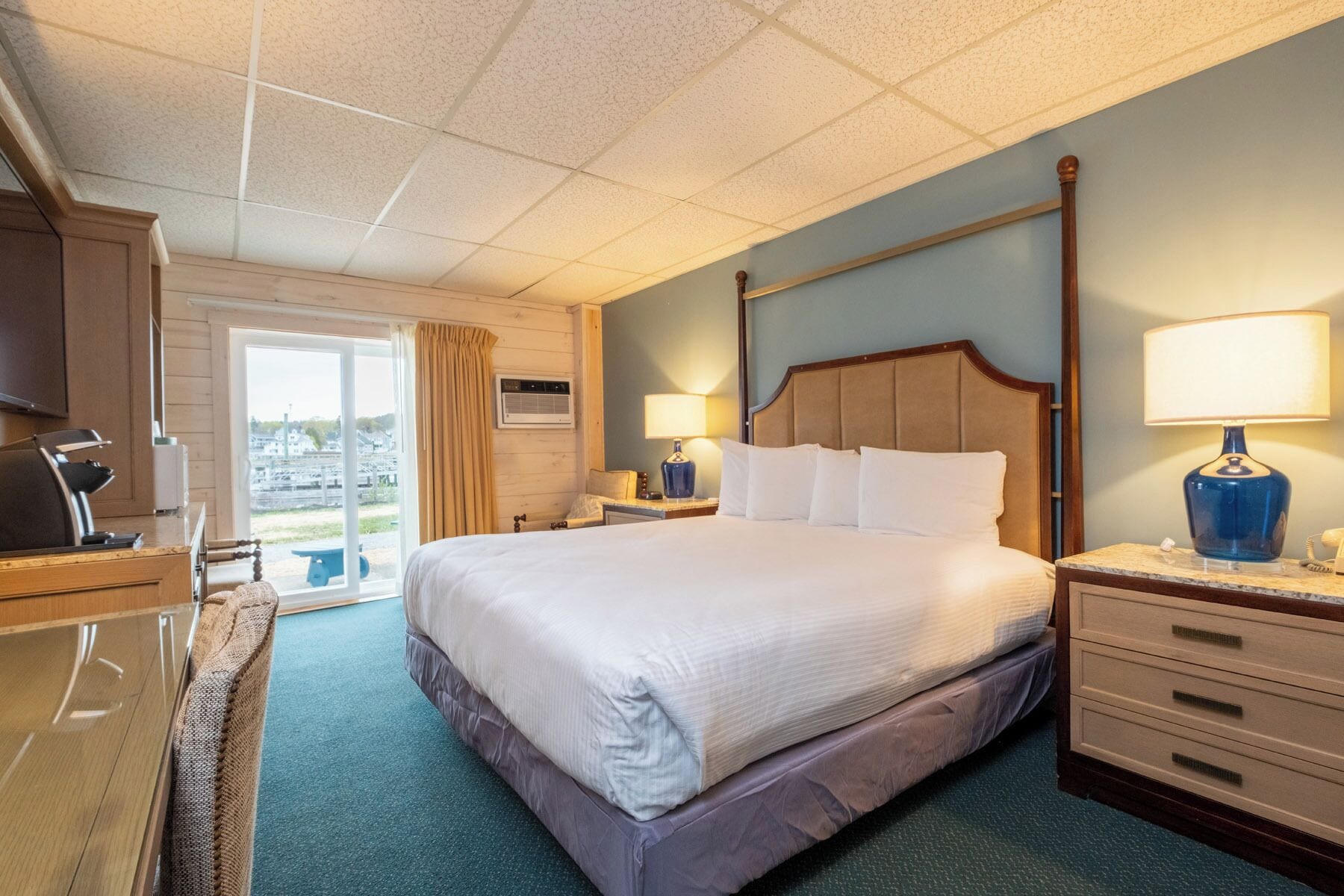 Une chambre d’hôtel avec un grand lit, un bureau avec une chaise, une table de chevet avec une lampe et une vue sur l’extérieur.